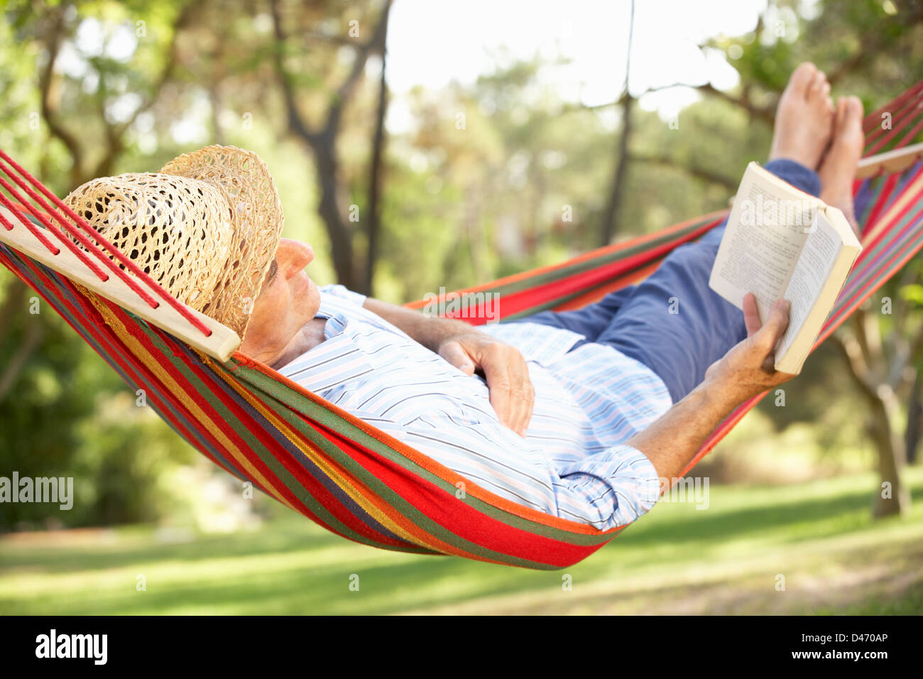 Senior Woman Relaxing In Hammock With Book Banque D'Images
