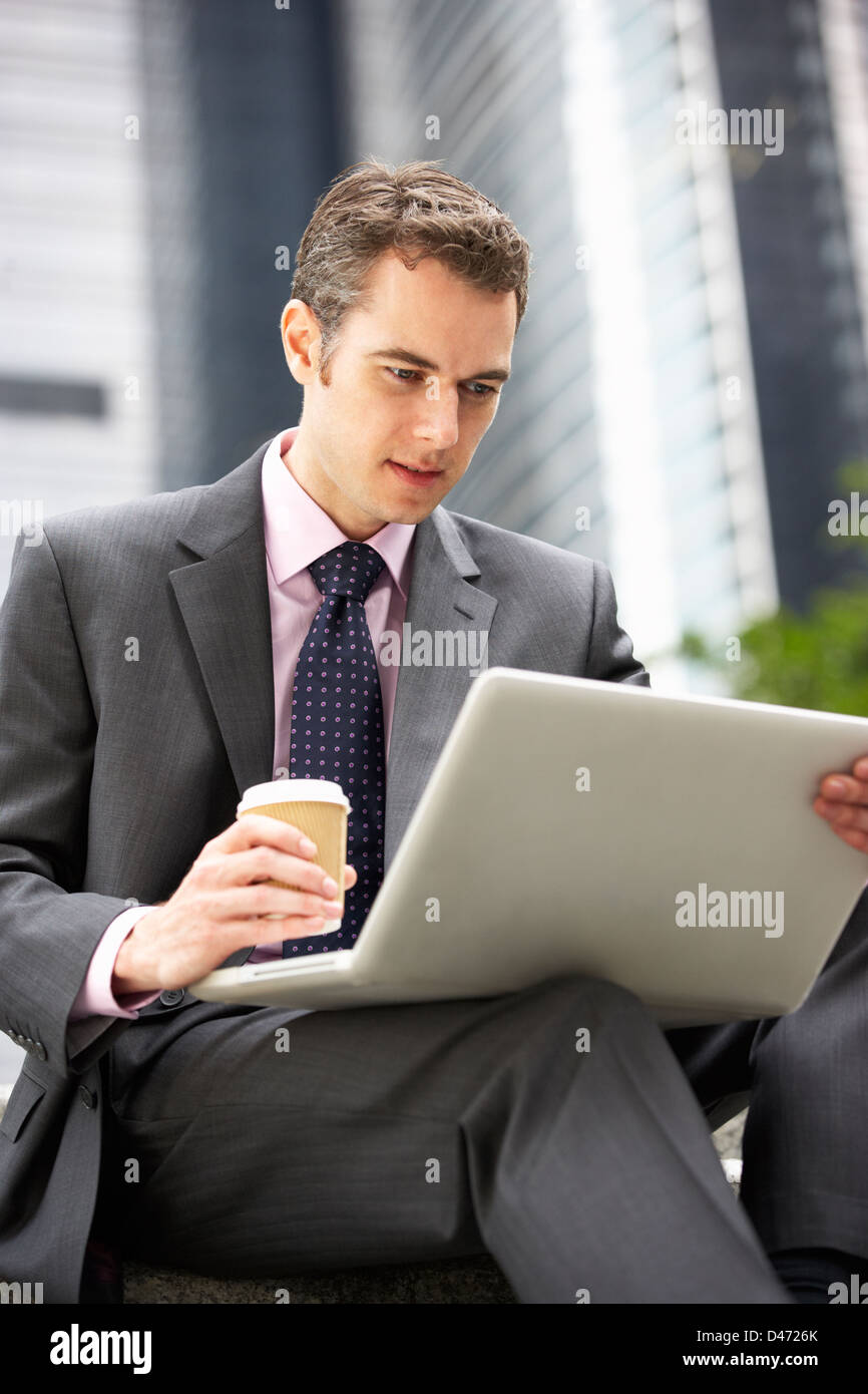 Businessman Working On Laptop à l'extérieur du bureau avec du café à emporter Banque D'Images