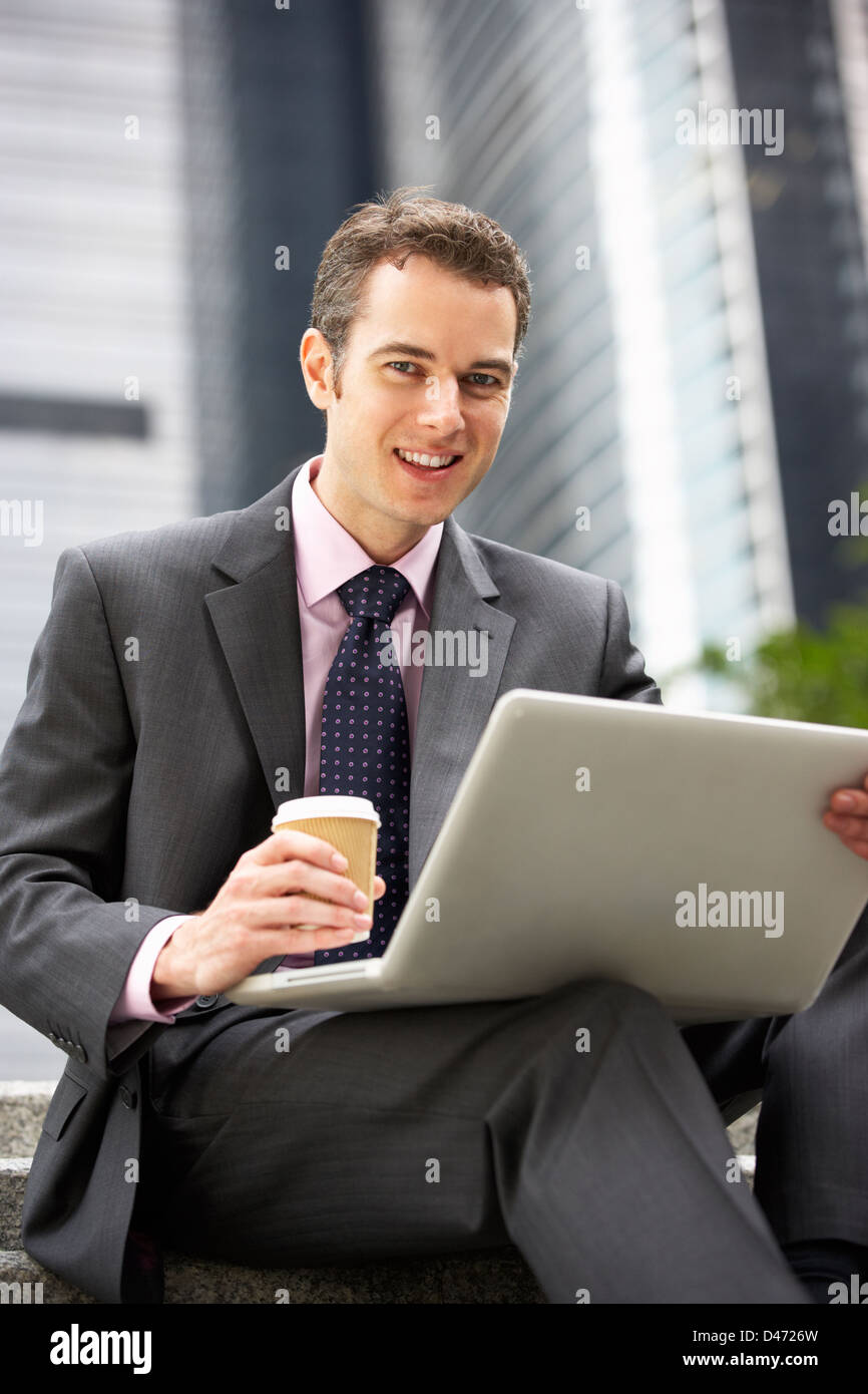 Businessman Working On Laptop à l'extérieur du bureau avec du café à emporter Banque D'Images