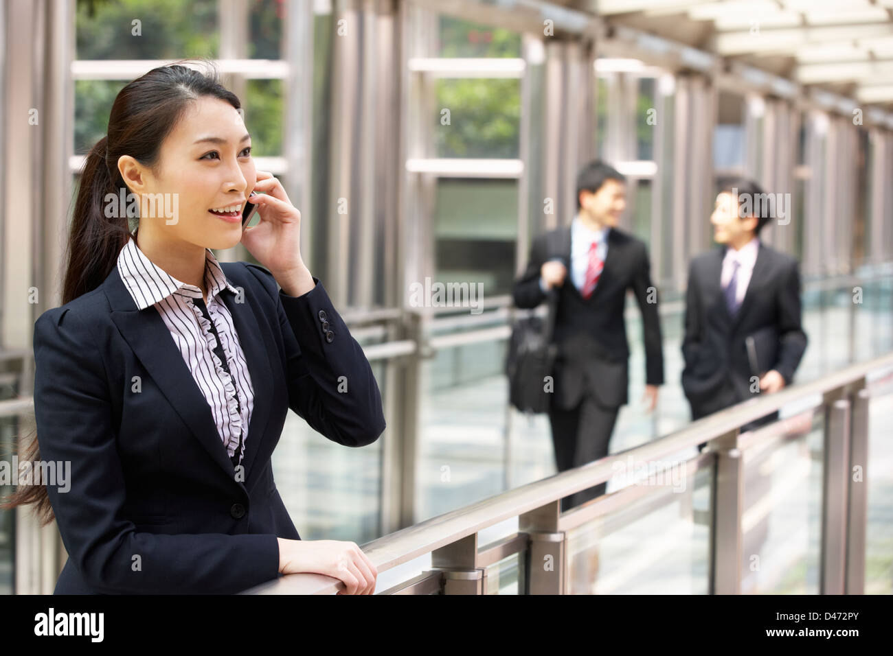 Chinese Businesswoman Outside Office sur téléphone mobile avec ses collègues en arrière-plan Banque D'Images