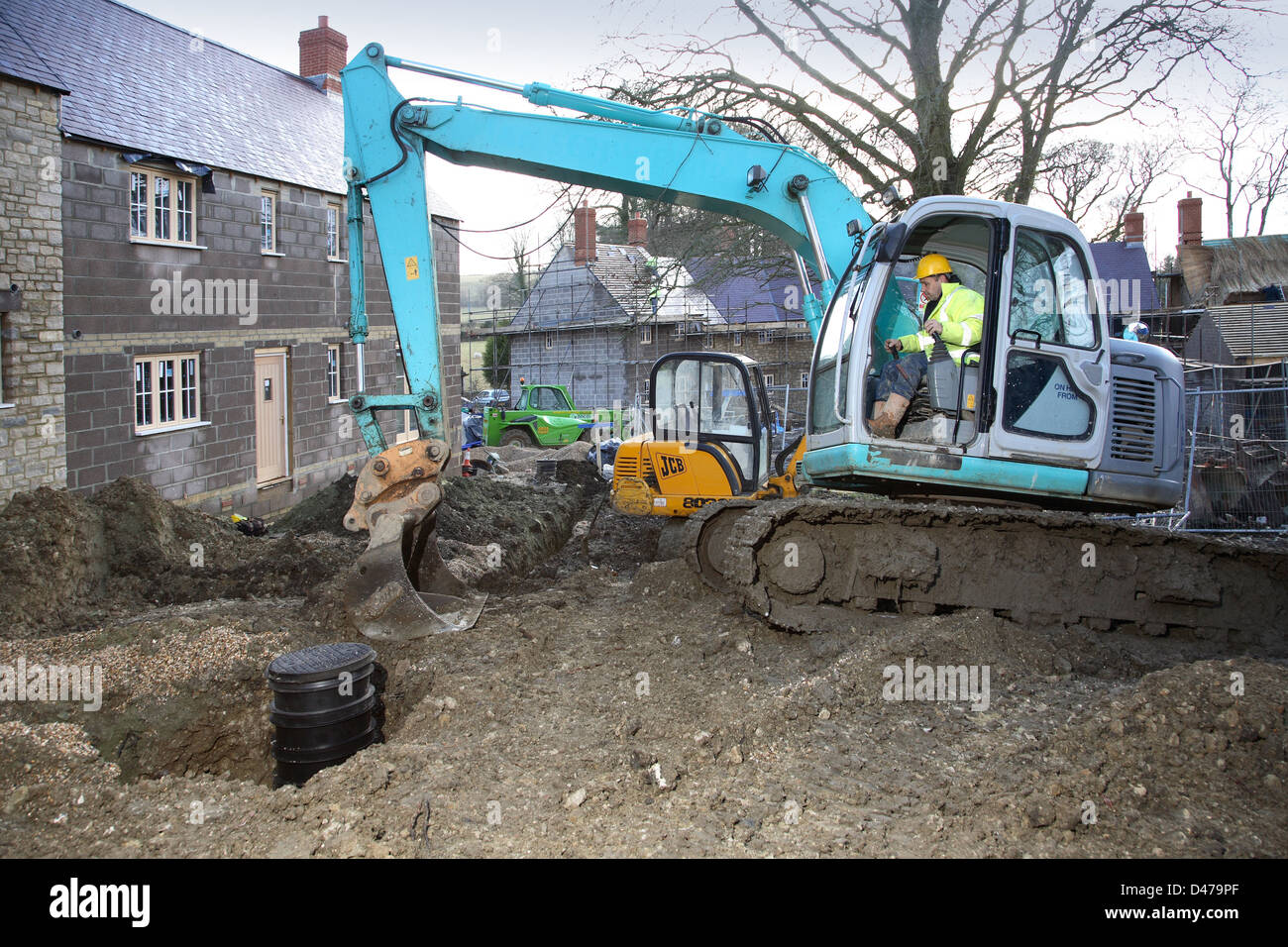 Un ouvrier utilise une pelle mécanique lors de l'installation de tuyaux de drainage sur un développement du logement traditionnel dans le Dorset, UK Banque D'Images