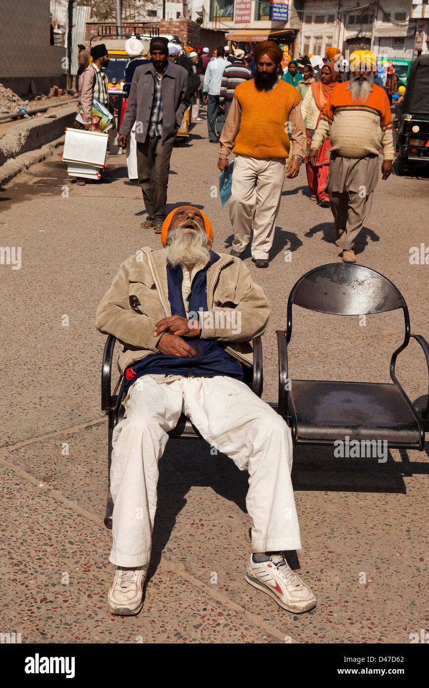 Un homme endormi sur un siège à Amritsar avec scène de foule colorée Banque D'Images