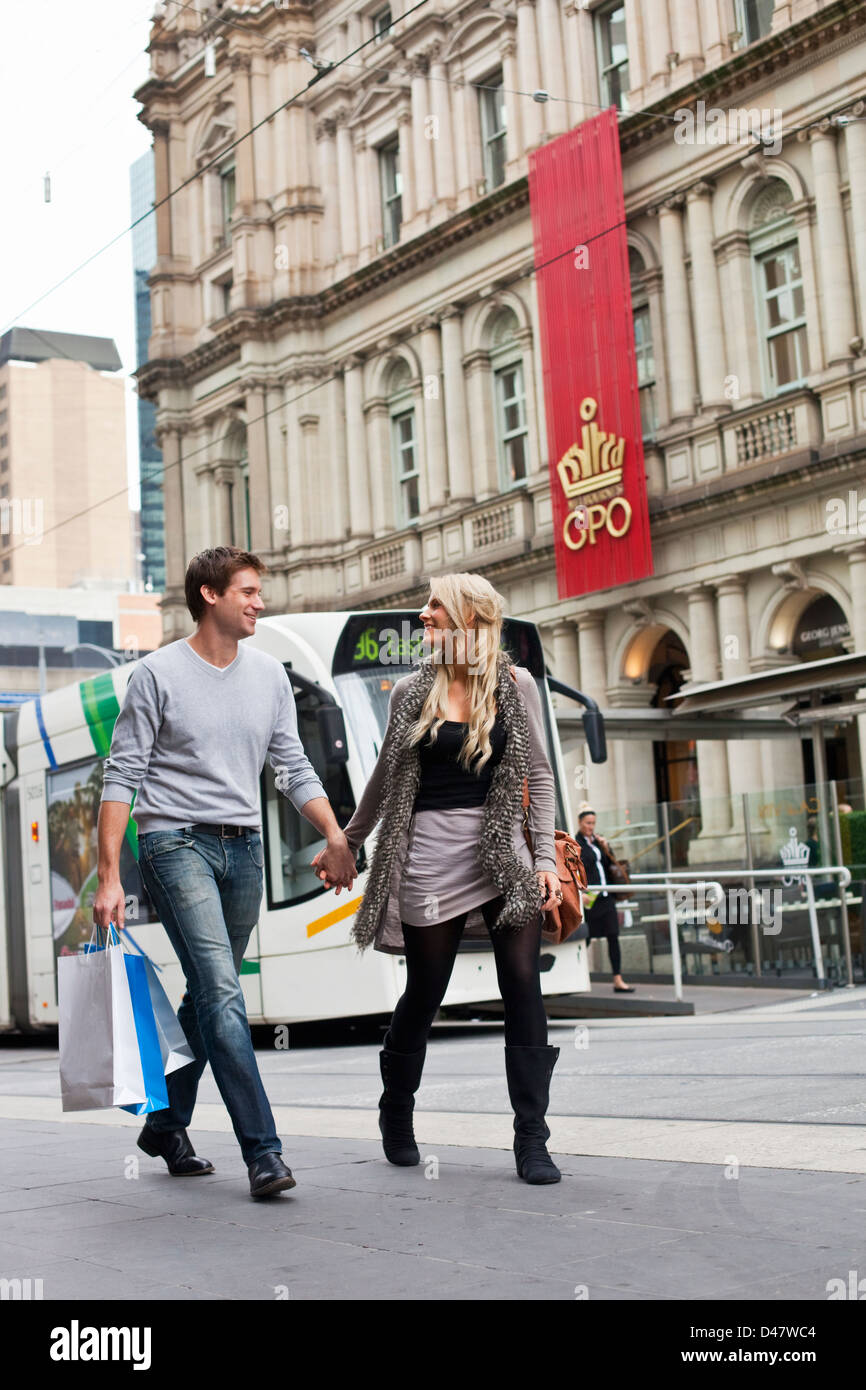 Jeune couple carrying shopping bags, avec le tram de la ville en arrière-plan. Bourke Street Mall, Melbourne, Victoria, Australie Banque D'Images