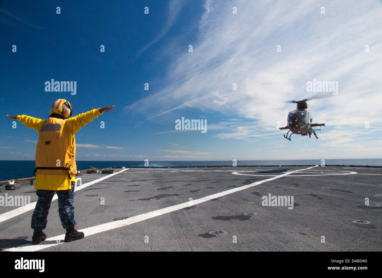 Un marin de l'US Navy guide un hélicoptère sur le pont d'envol d'un navire de la marine dans l'océan Atlantique. Cette opération fait partie des opérations standard du poste de pilotage, assurant que l'hélicoptère est correctement positionné pour le décollage ou l'atterrissage, soutenant les missions aériennes de la Marine. Banque D'Images