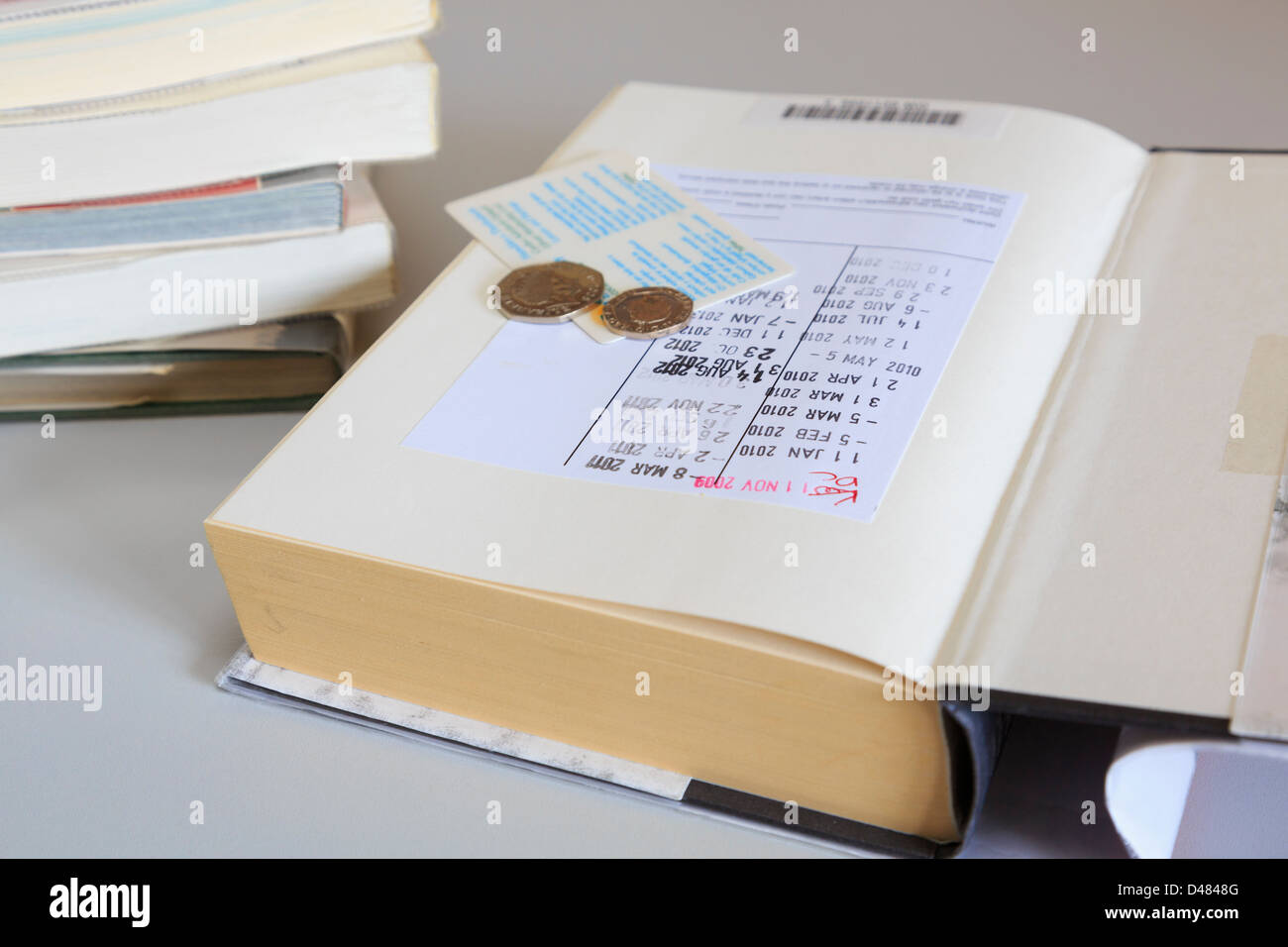 Ouvrir des livres de bibliothèque sur la première page avec les dates de retour, le cachet du service de carte de membre et des pièces pour une amende. Royaume-uni Grande-Bretagne Banque D'Images