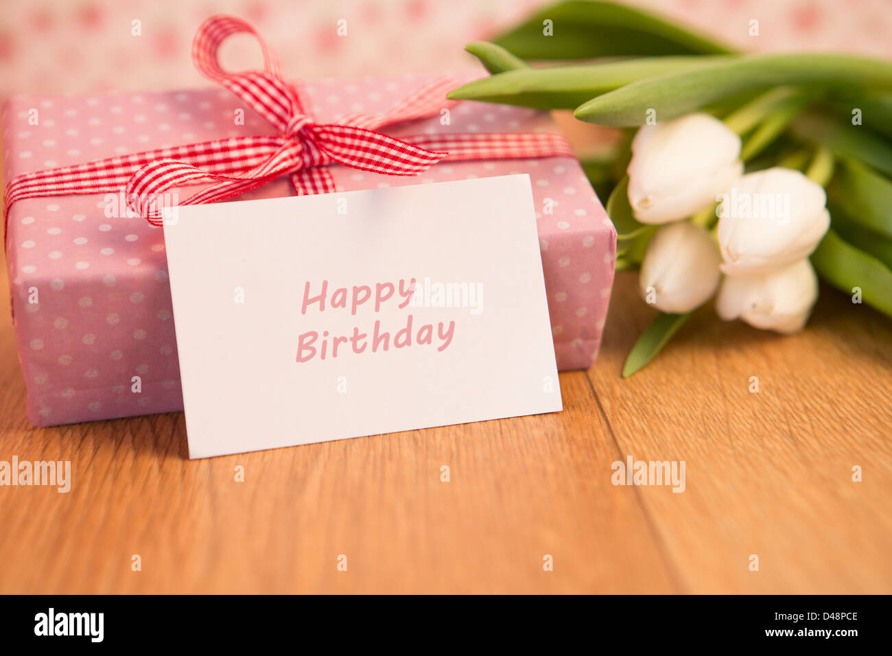 Pink wrapped present avec bouquet de tulipes blanches et happy birthday card Banque D'Images