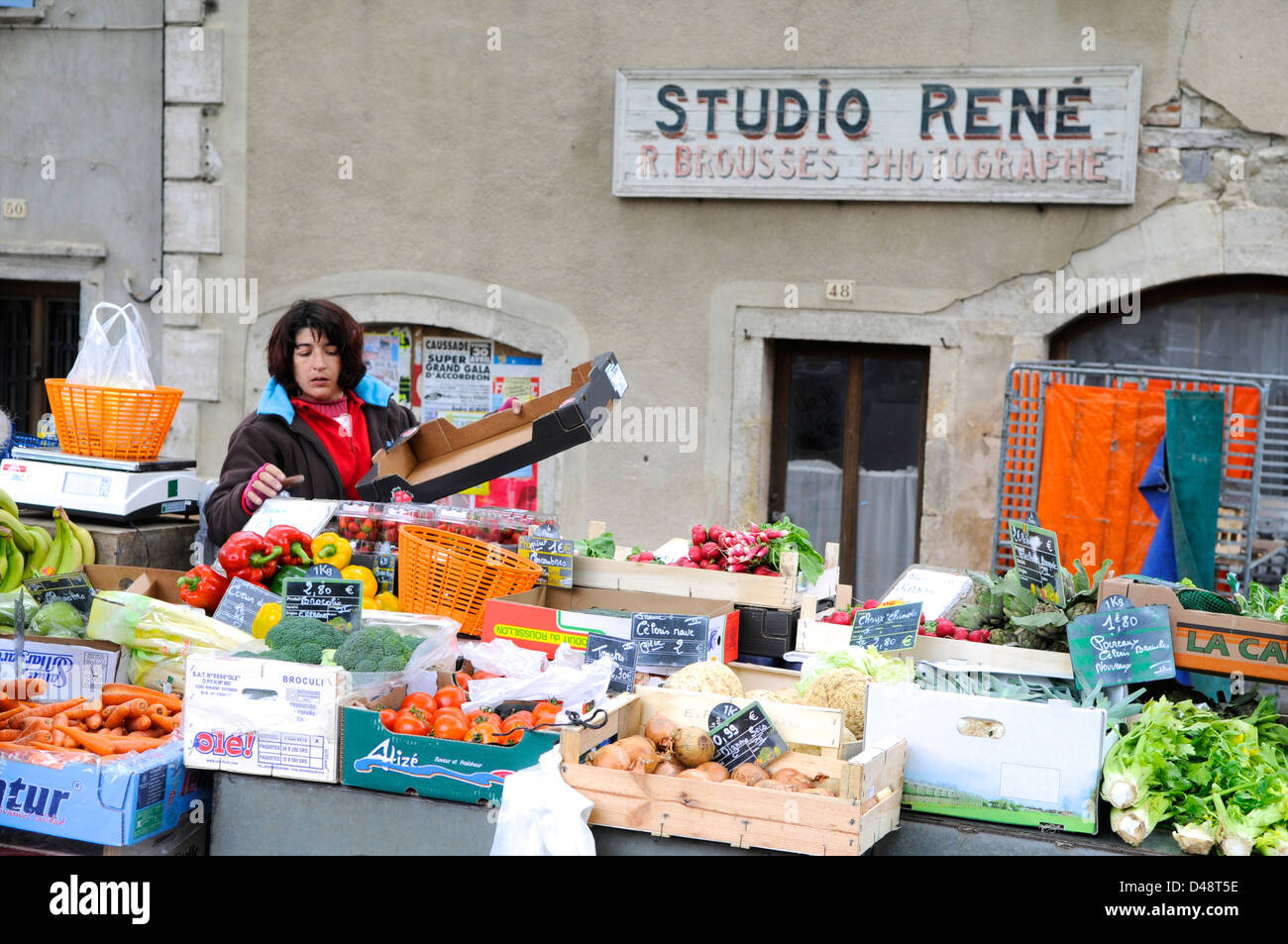 Femme vendant des légumes sur le marché à l'extérieur d'un ancien studio de photographie. Saint-Antonin-Noble-Val, Tarn et Garonne, France Banque D'Images