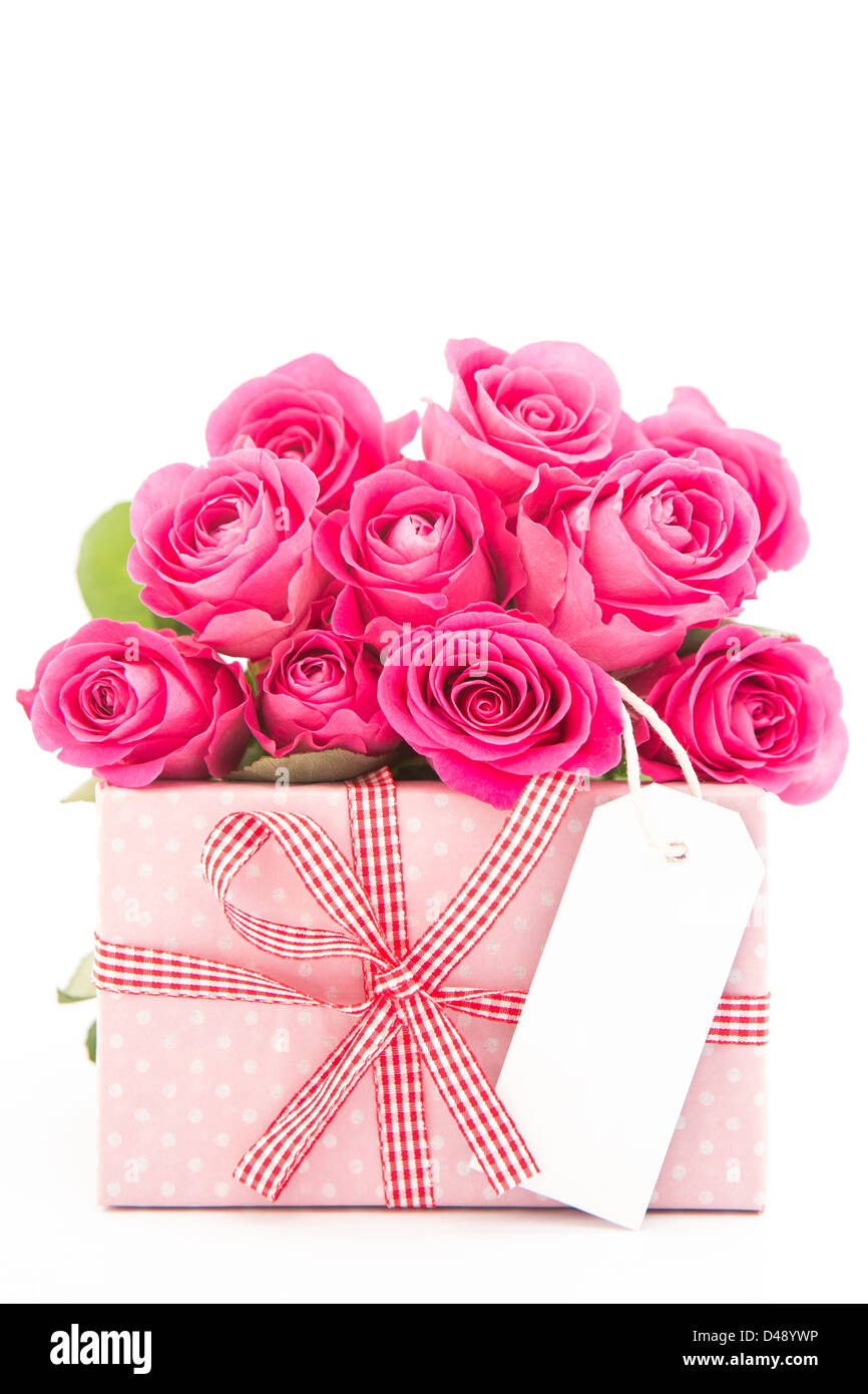 Bouquet de belles roses à côté d'un cadeau rose avec une carte vierge sur fond blanc Banque D'Images
