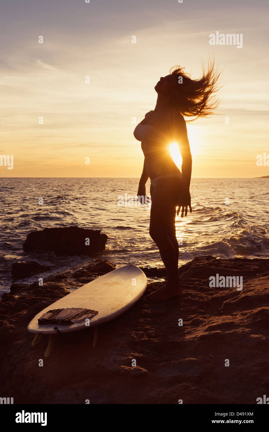 Silhouette d'une femme debout sur un rocher au bord de l'eau avec sa planche de surf au coucher du soleil;Tarifa cadiz andalousie espagne Banque D'Images