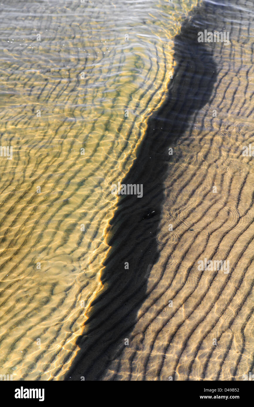 Une petite vague roule sur le sable ondulée sur une plage de sable ensoleillée Banque D'Images