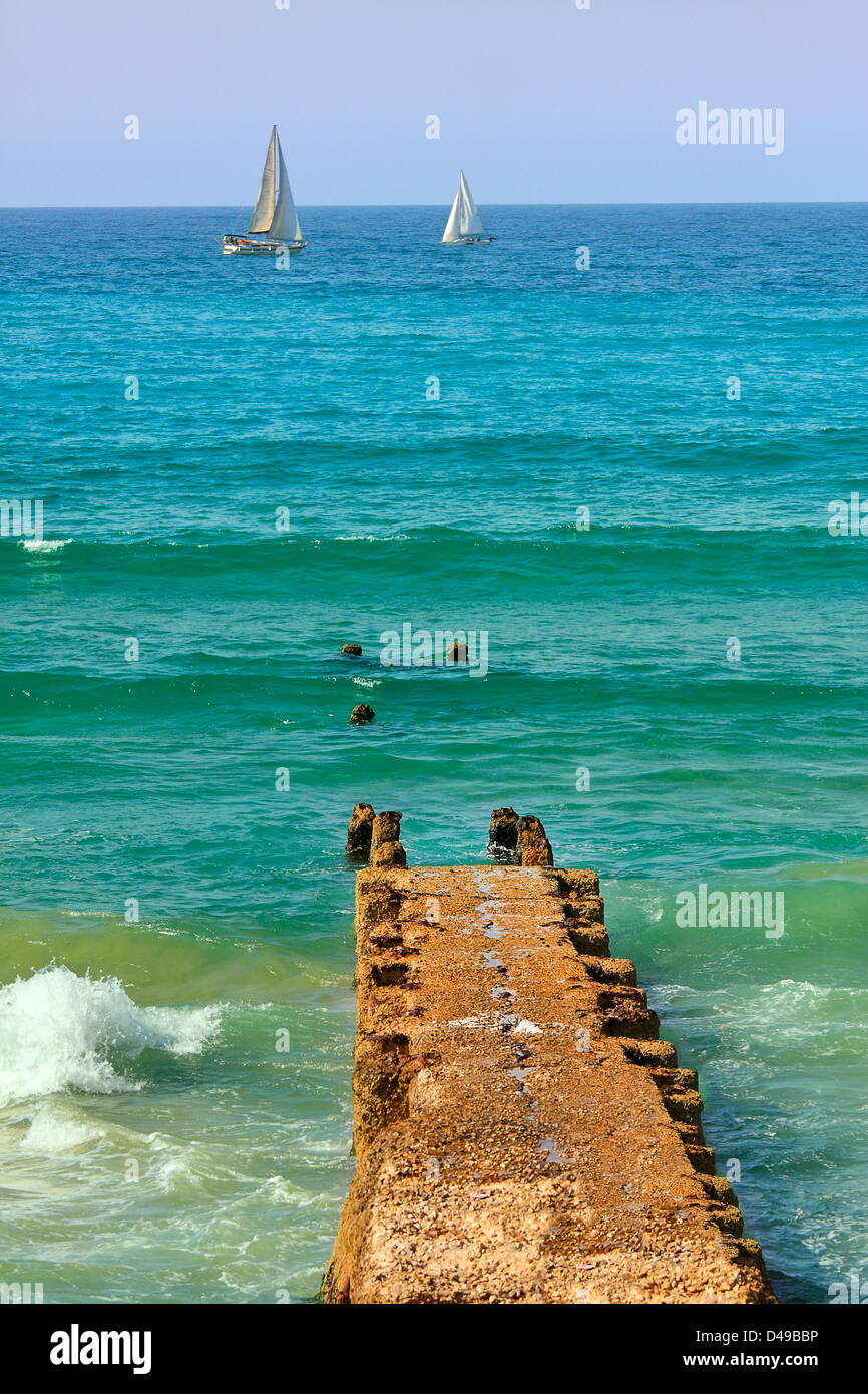 L'image de vieux orientée verticale jetée ruinée sur la mer Méditerranée et deux yachts sur contexte en Israël. Banque D'Images