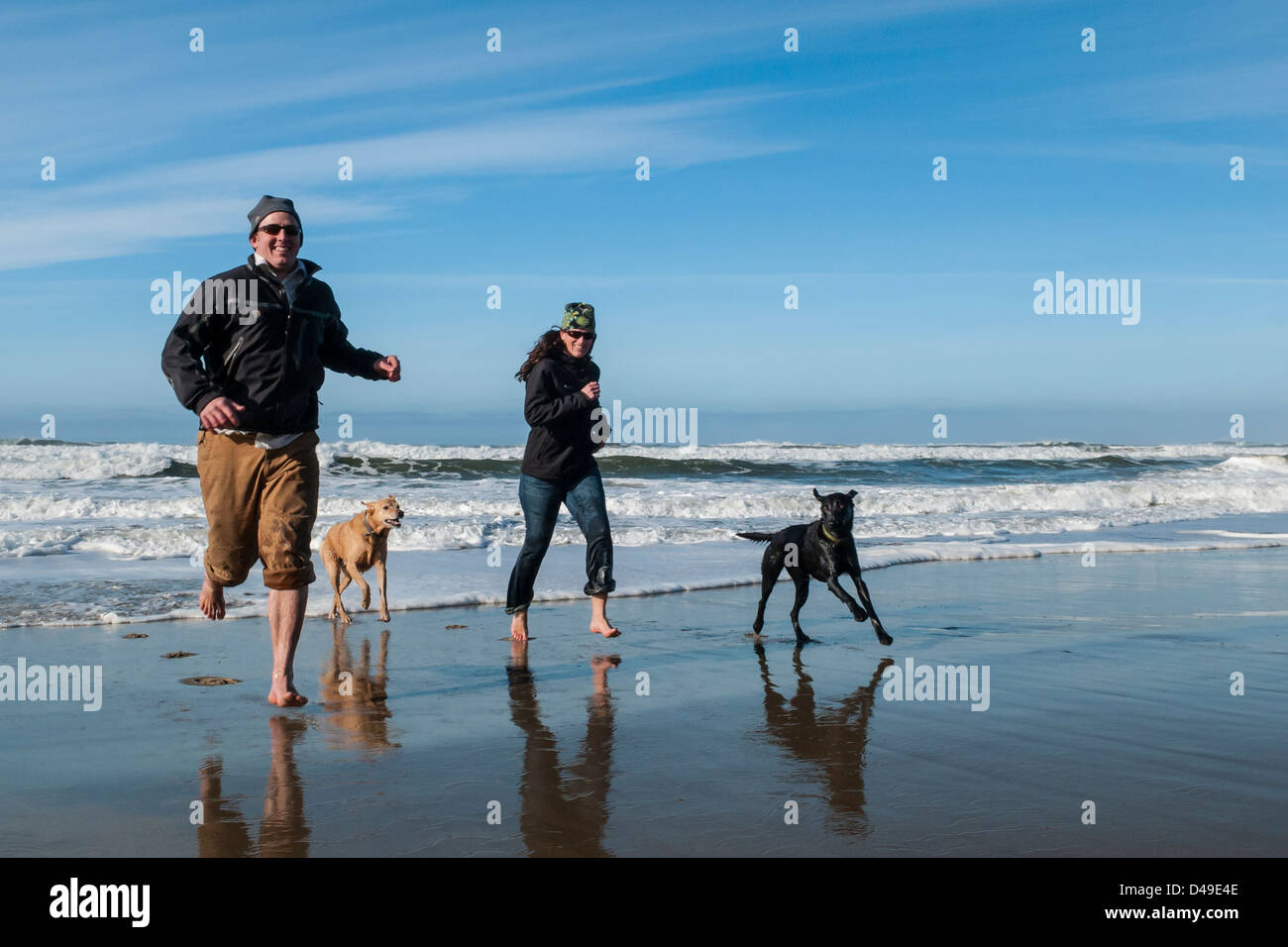 Jeune couple adulte et chiens courant sur la plage dans l'Oregon Dunes National Recreation Area. Banque D'Images