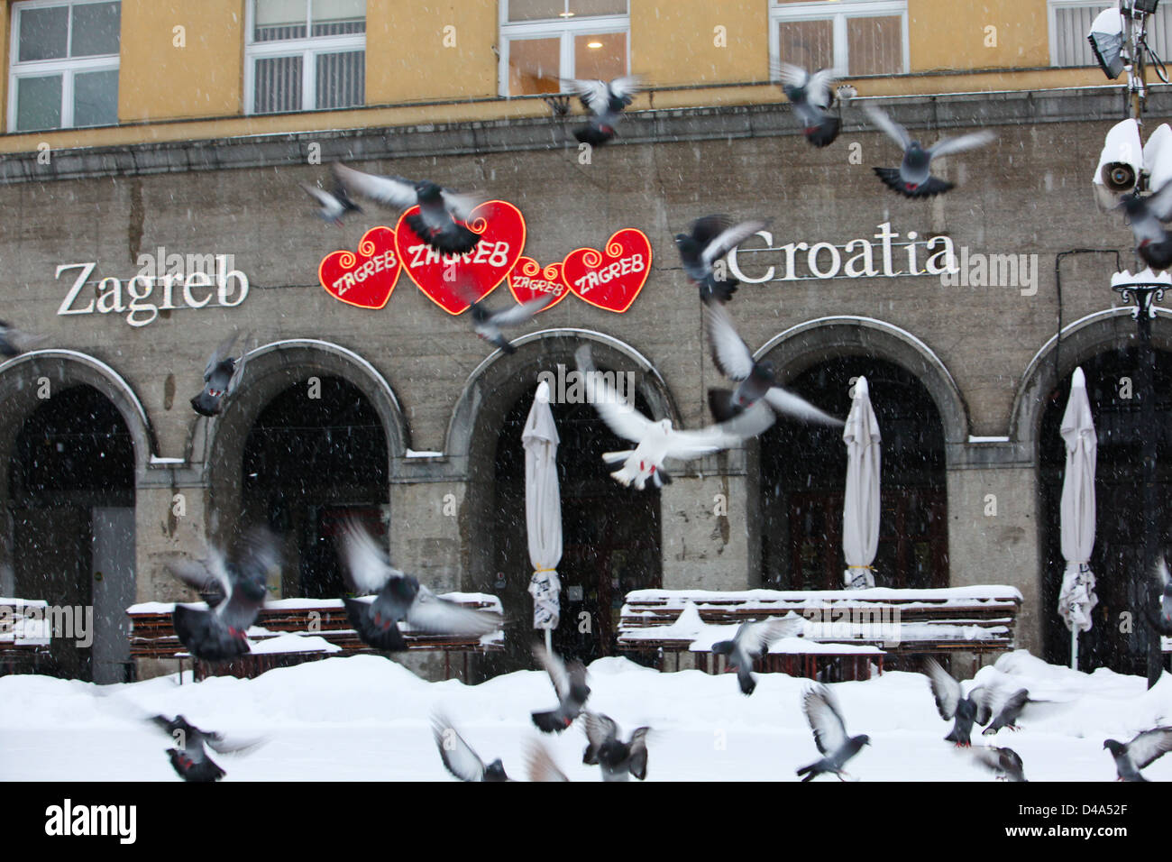 Les pigeons voler jusqu'au square couvert de neige en face du bâtiment. Banque D'Images