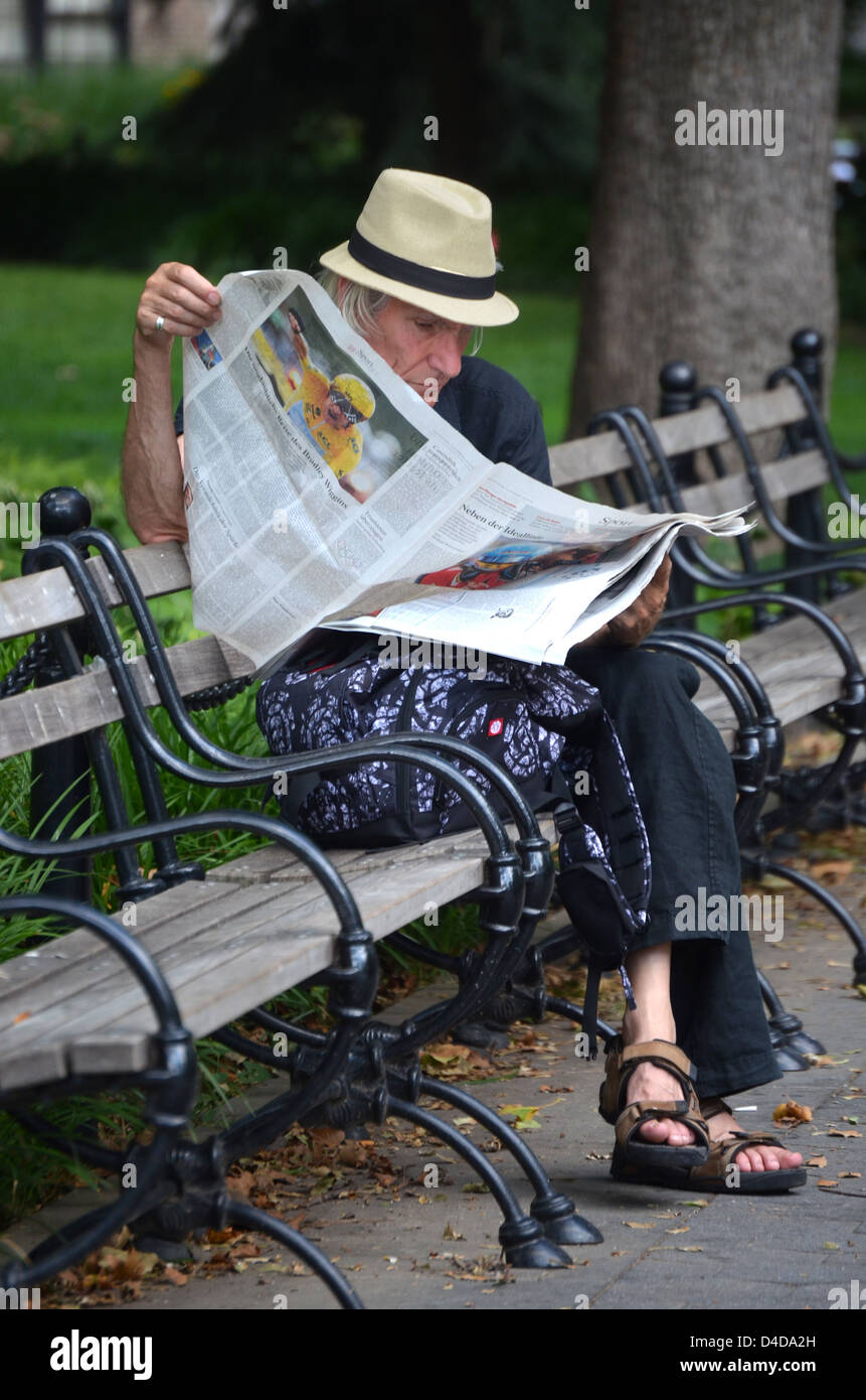 L'homme en sandales la lecture d'un journal quotidien à Washington Square Park à Greenwich Village, New York City. Banque D'Images