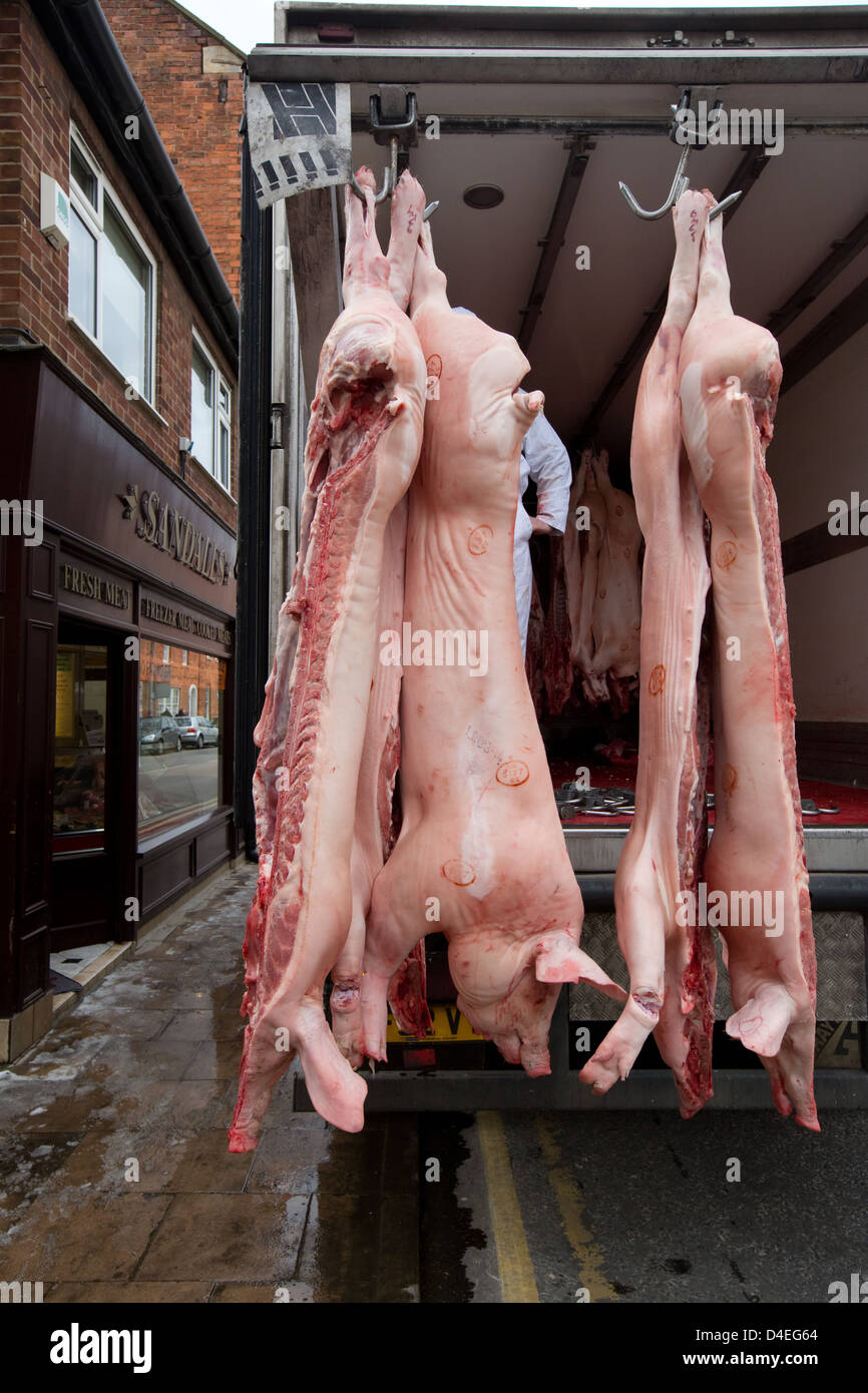 Des carcasses de porc étant déchargé d'un camion frigorifique en un High Street Butchers Shop Banque D'Images