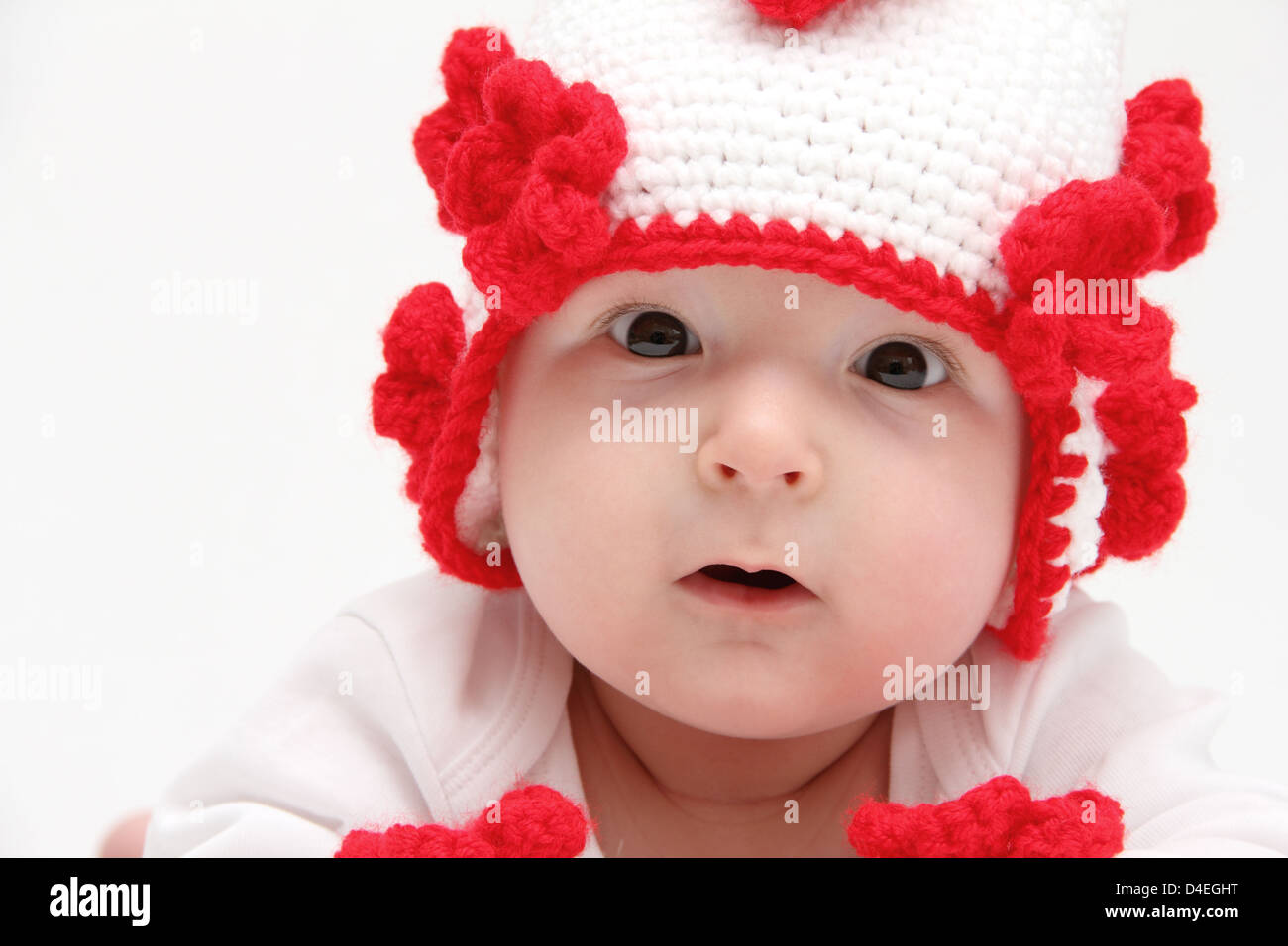 Petit bébé avec chapeau blanc tricoté avec les fleurs rouges Banque D'Images