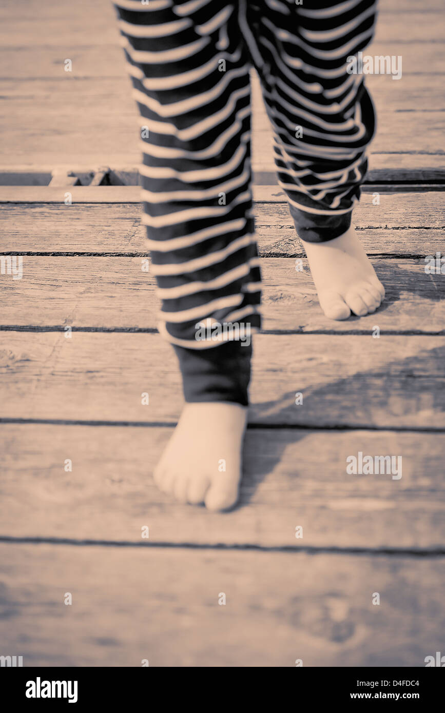 Jambes et Pieds de bébé fille qui marche pieds nus sur la jetée en bois Banque D'Images