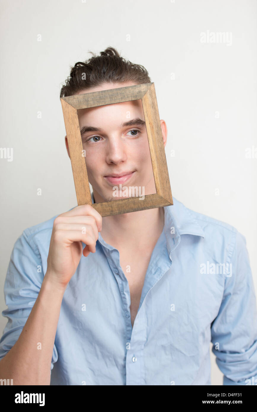 Heureux et insouciant jeune adulte homme posant avec cadre en bois en face de son visage Banque D'Images
