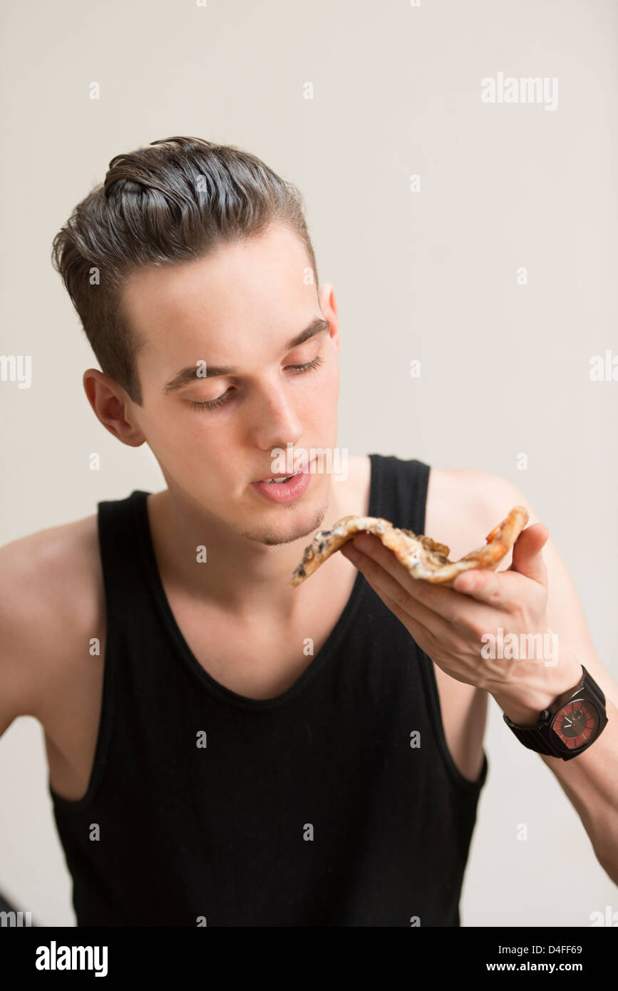Jeune adulte homme portant un débardeur noir et eating pizza Banque D'Images