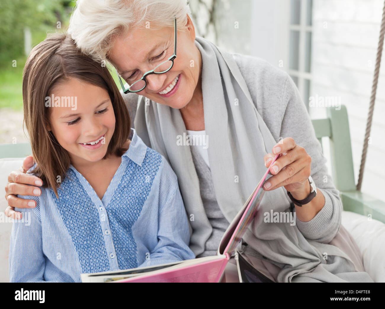 Petite-fille et femme lecture le porche swing Banque D'Images