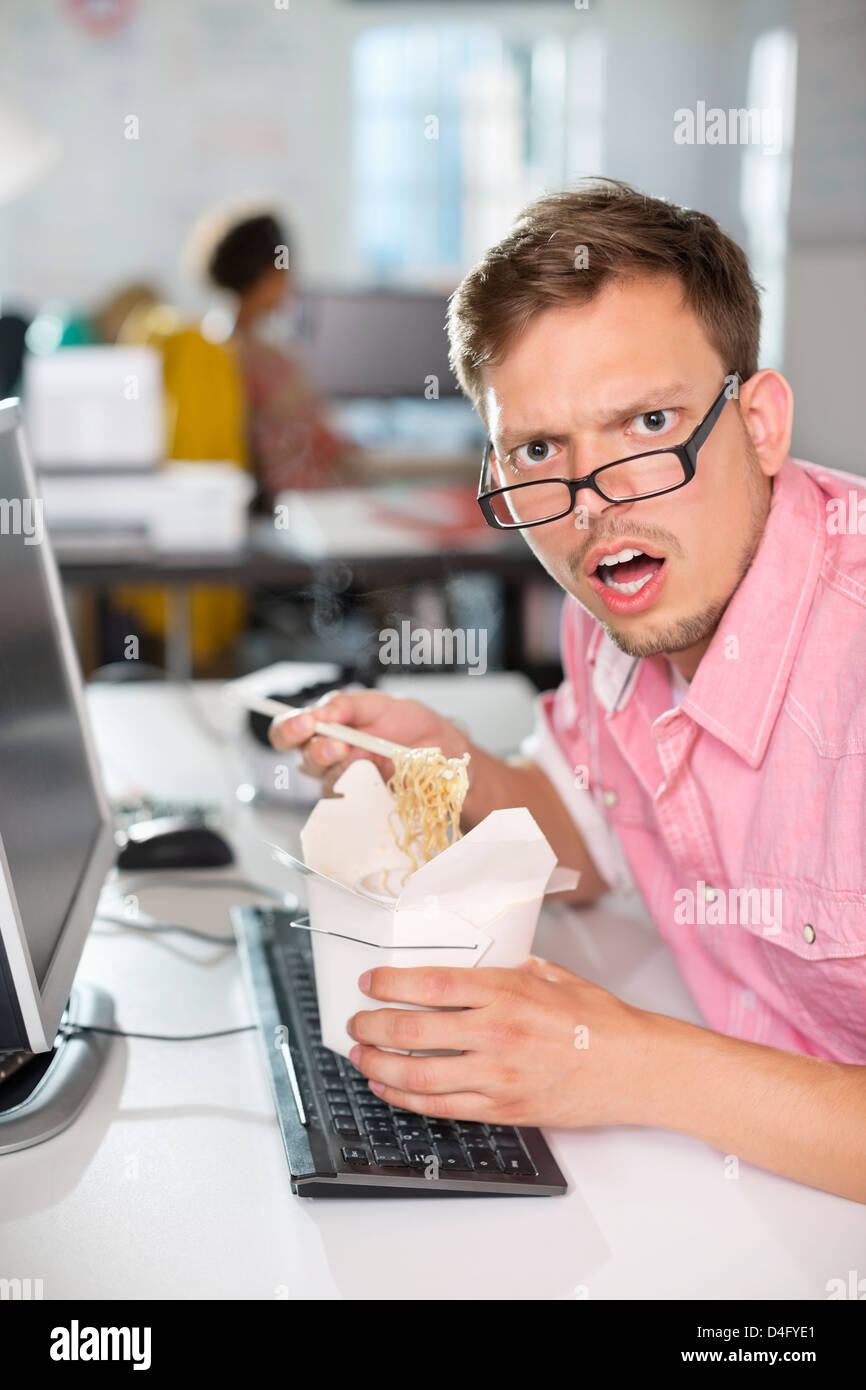 Businessman eating Chinese food at desk Banque D'Images