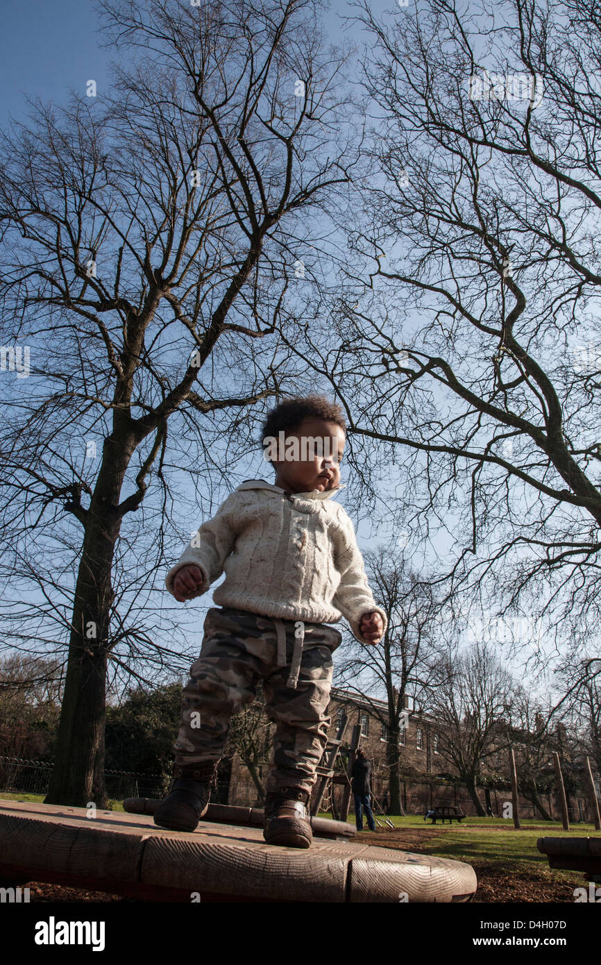 Mixed Race bébé garçon en stationnement debout sur le tableau, le port de cavalier crème d'arbres en arrière-plan Banque D'Images