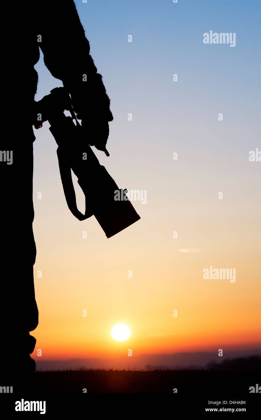 La photographe d'un appareil photo avec un objectif grand au lever du soleil. Silhouette Banque D'Images