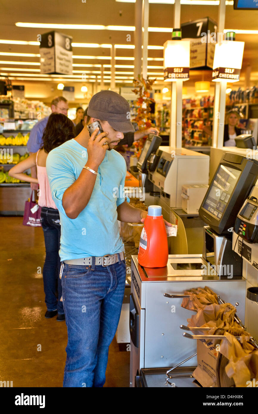 Tout en faisant un achat de supermarché, un jeune hispanique des profils de scanner un code barre d'escompte coupon à une borne de libre-encaissement Banque D'Images