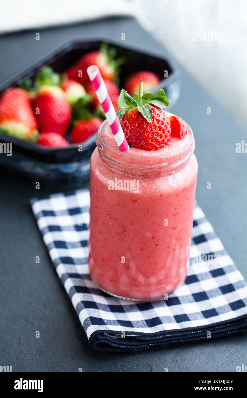 Gros plan du smoothie aux fruits fraise et le bac de fraises fraîches en arrière-plan Banque D'Images