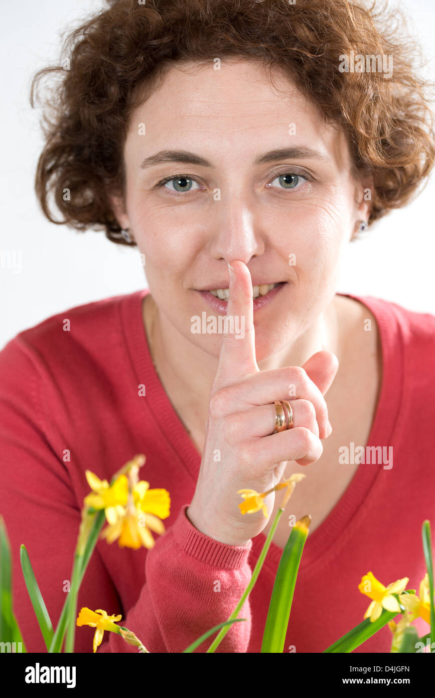 Jeune femme avec des cheveux bouclés et pull rouge du doigt de maintien en face de ses lèvres Banque D'Images