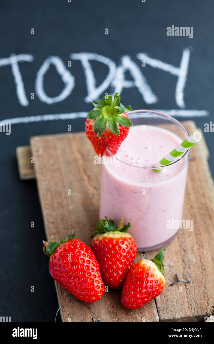 Smoothie aux fraises de paille à rayures et de fraises entières sur le plateau de service en bois Banque D'Images