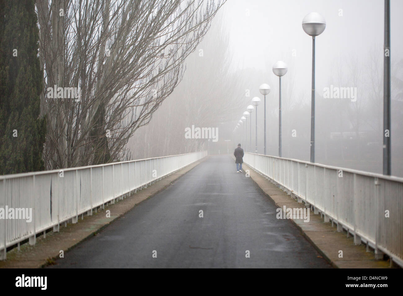 Un homme traverse un pont au-dessus d'un lac un jour brumeux Banque D'Images