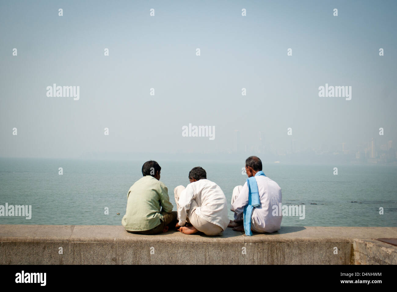 Trois hommes Indiens assis sur le mur de la mer donnant sur la mer d'Oman à chowpatti beach, Mumbai, Inde Banque D'Images
