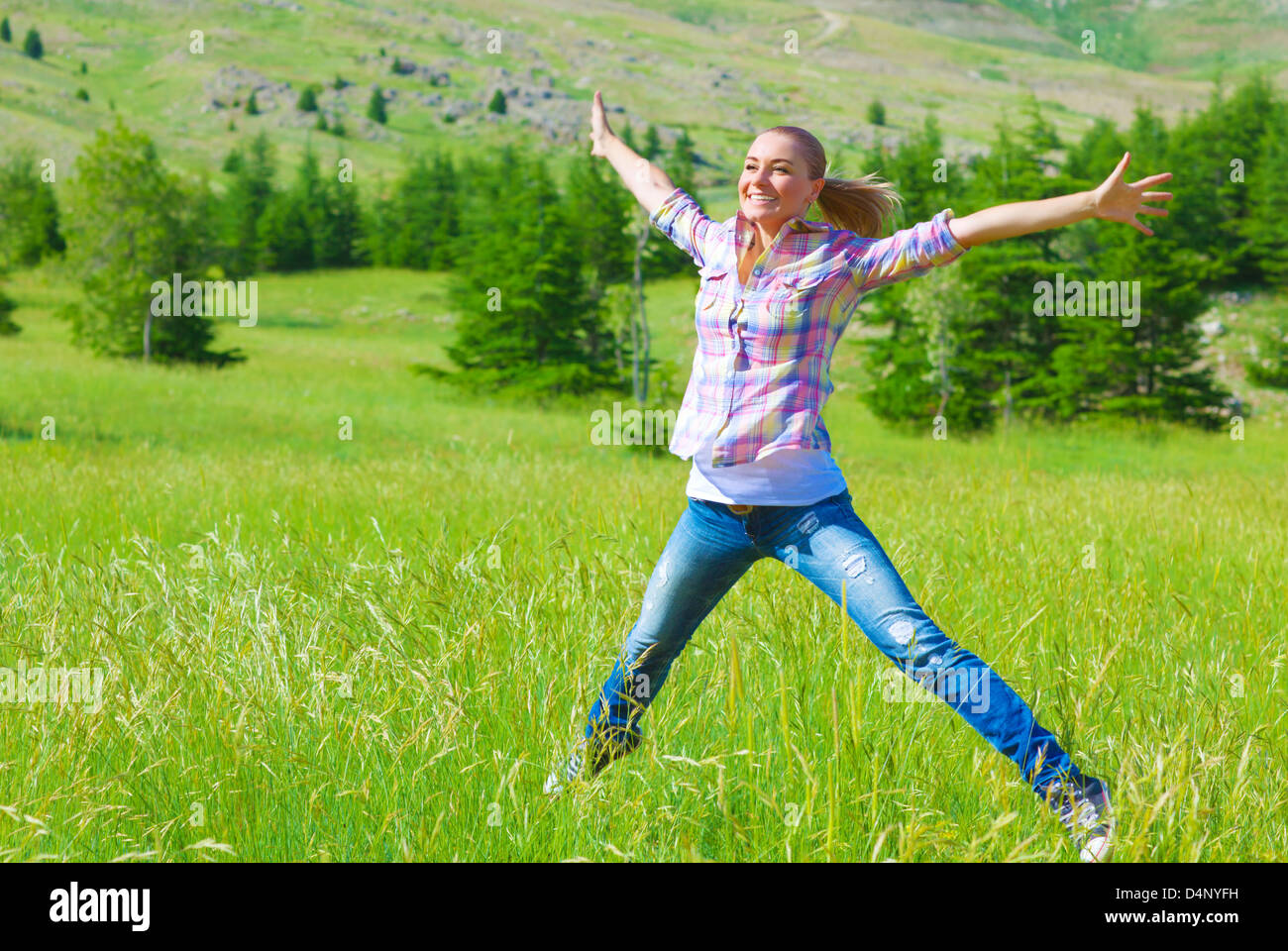Happy girl de sauter sur le terrain, profitant de l'air frais et l'herbe verte du printemps, la liberté et le bonheur concept Banque D'Images