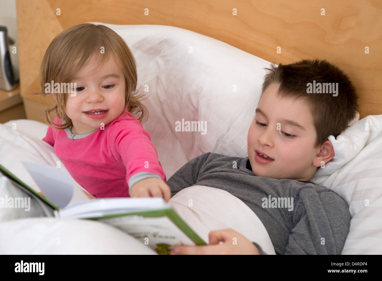 Petite soeur de braquer une page à son frère aîné dans le livre avant d'aller dormir. Banque D'Images