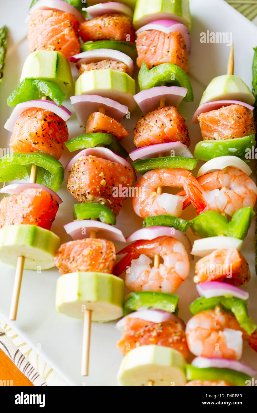 Cubes de saumon et de crevettes a complimenté avec légumes sur les brochettes. Prêt à cuire. Oignons rouges, courgettes et poivrons verts. Banque D'Images