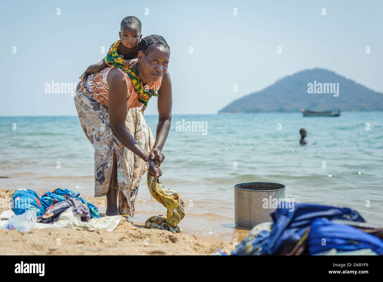 Femme avec enfant lave des vêtements sur la rive du lac Malawi, Malawi, Afrique Banque D'Images