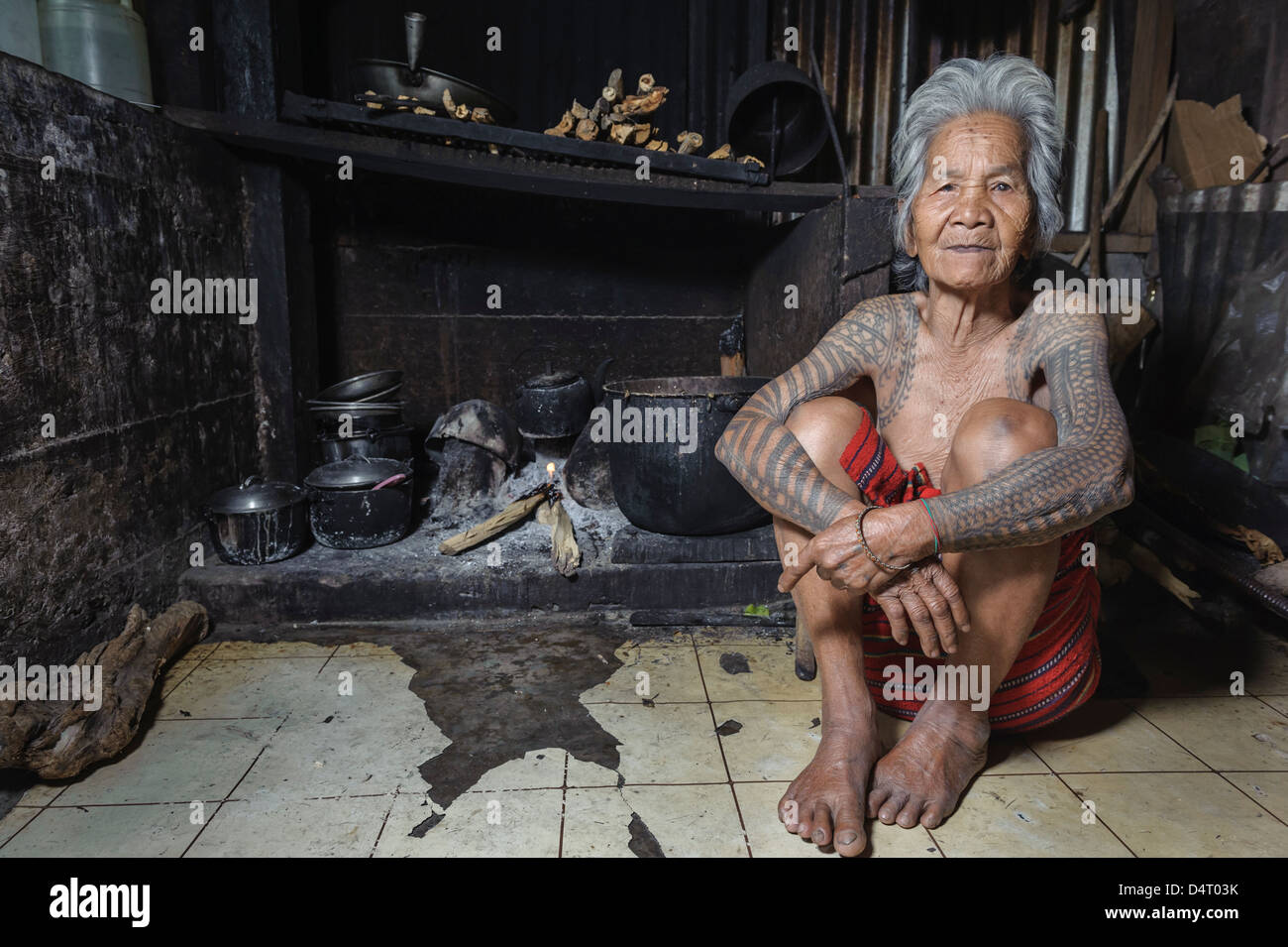 Le BSL femme tatouée de Tinglayan assis près de la cheminée, Luzon, Philippines. Banque D'Images
