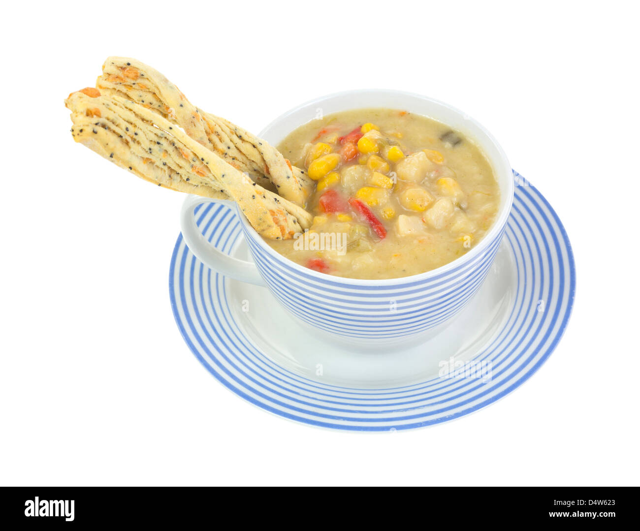 Une épaisse de chaudrée de maïs, pommes de terre et poivrons rouges dans une tasse et soucoupe rayé bleu avec craquelins torsadée inséré dans la soupe. Banque D'Images