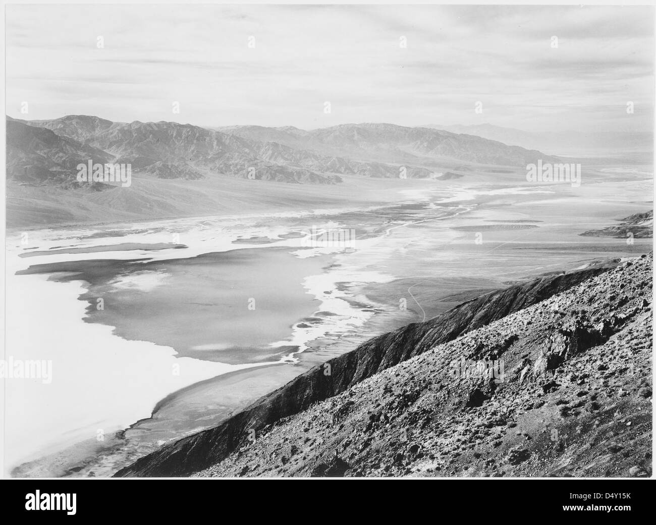 La photographie d'Ansel Adams capture le vaste paysage désertique du monument national de la Vallée de la mort en Californie. L'image regarde vers les montagnes lointaines, soulignant la beauté brutale de l'environnement désertique. Il reflète la maîtrise d'Adams dans la capture du paysage américain, en particulier les régions désertiques. Banque D'Images