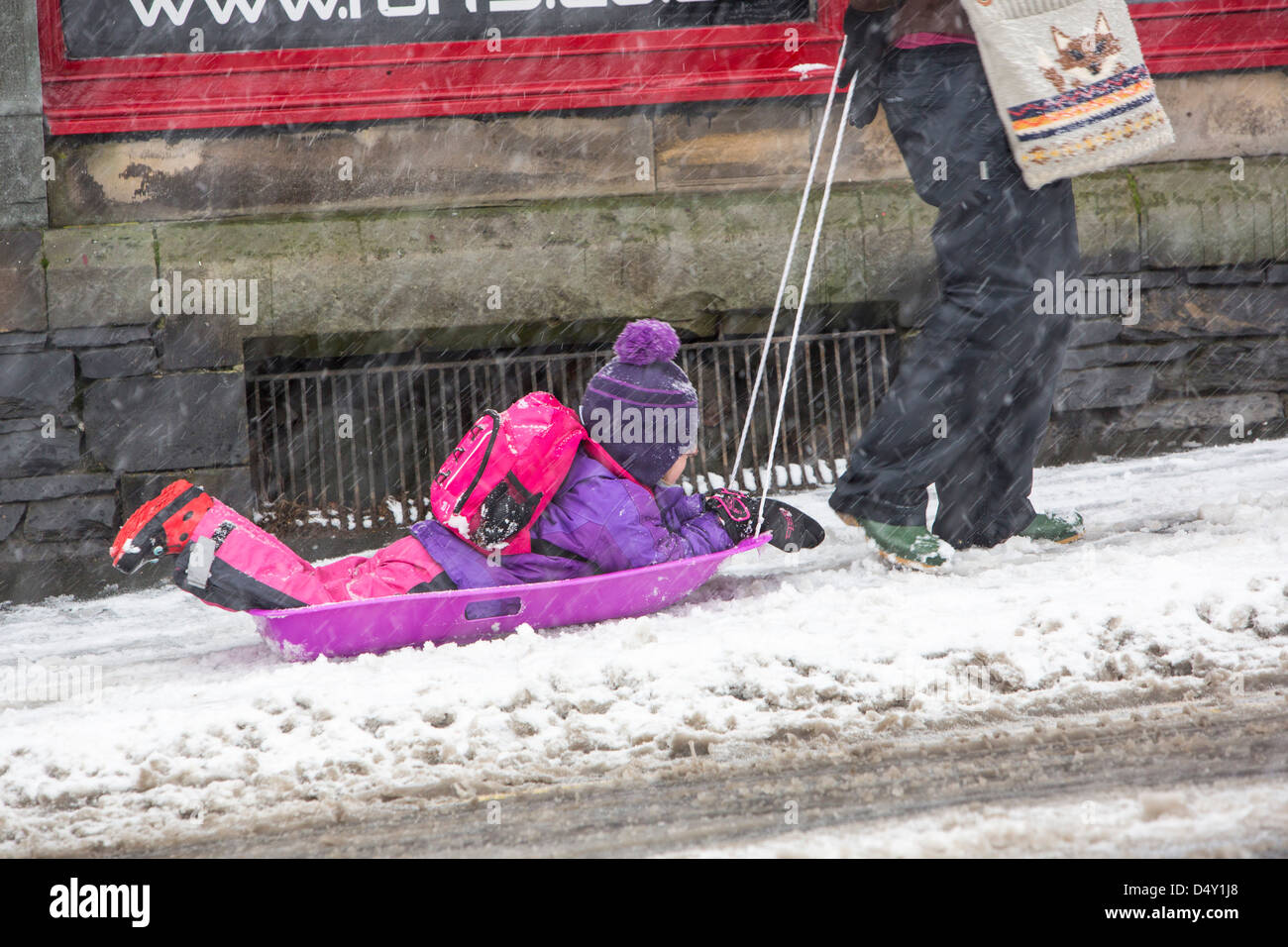 Un enfant d'être tiré sur un traîneau dans la neige à Ambleside, Lake District, UK. Banque D'Images