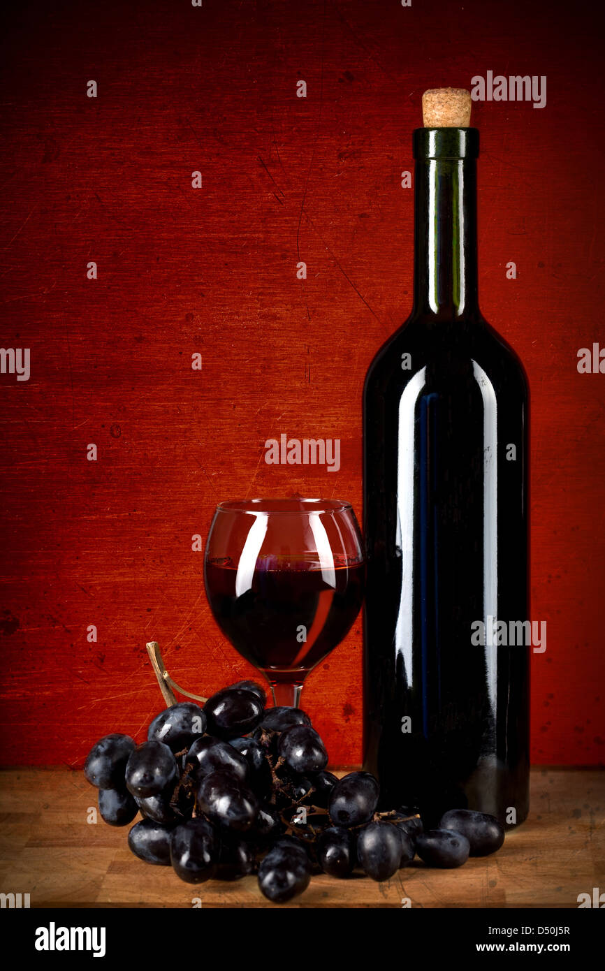 Bouteille de vin, le verre et les raisins sur rouge grunge background Banque D'Images