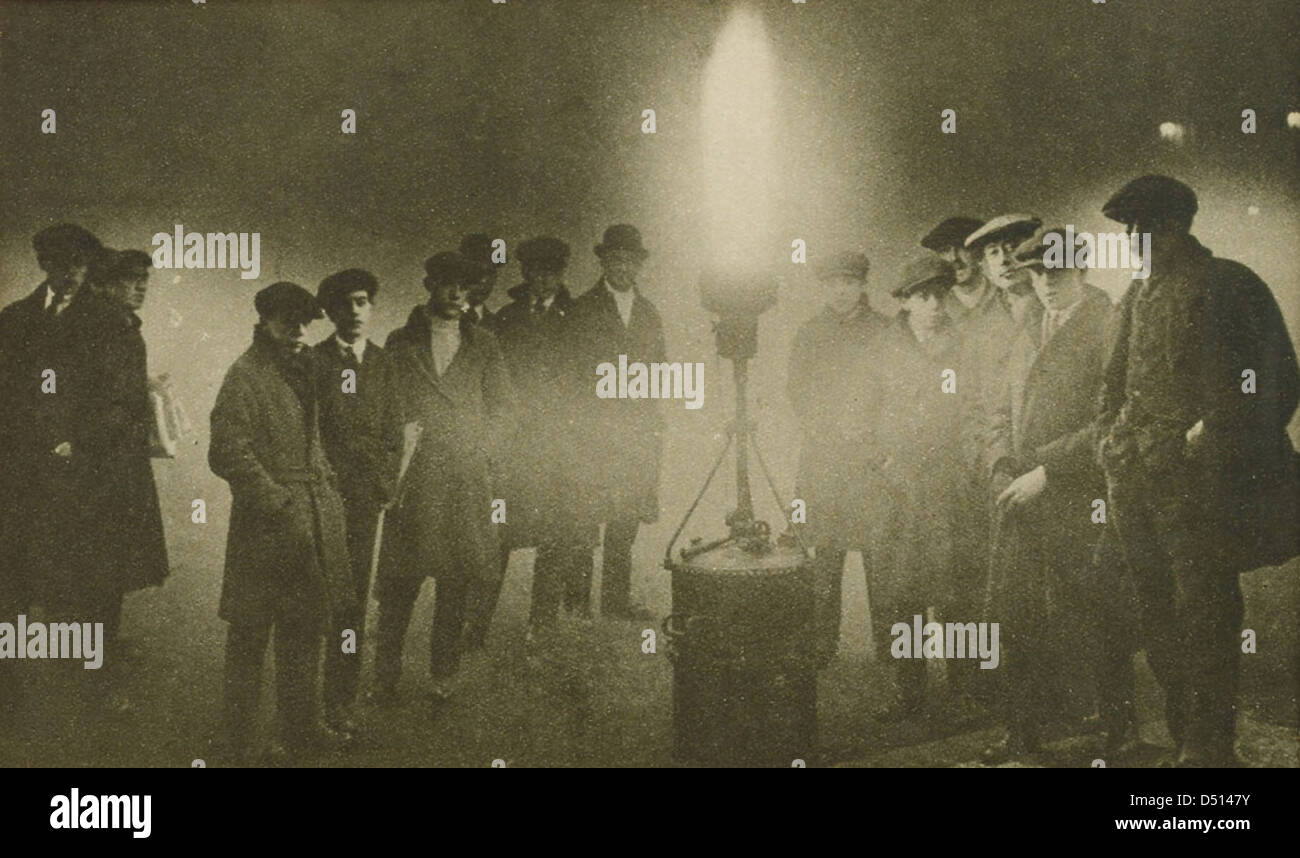 Une image historique d'hommes rassemblés autour d'une balise dans le smog épais, possiblement dans un endroit maritime. La photo met en lumière les conditions environnementales difficiles auxquelles sont confrontés les gens de mer et le rôle des balises dans la navigation. Banque D'Images