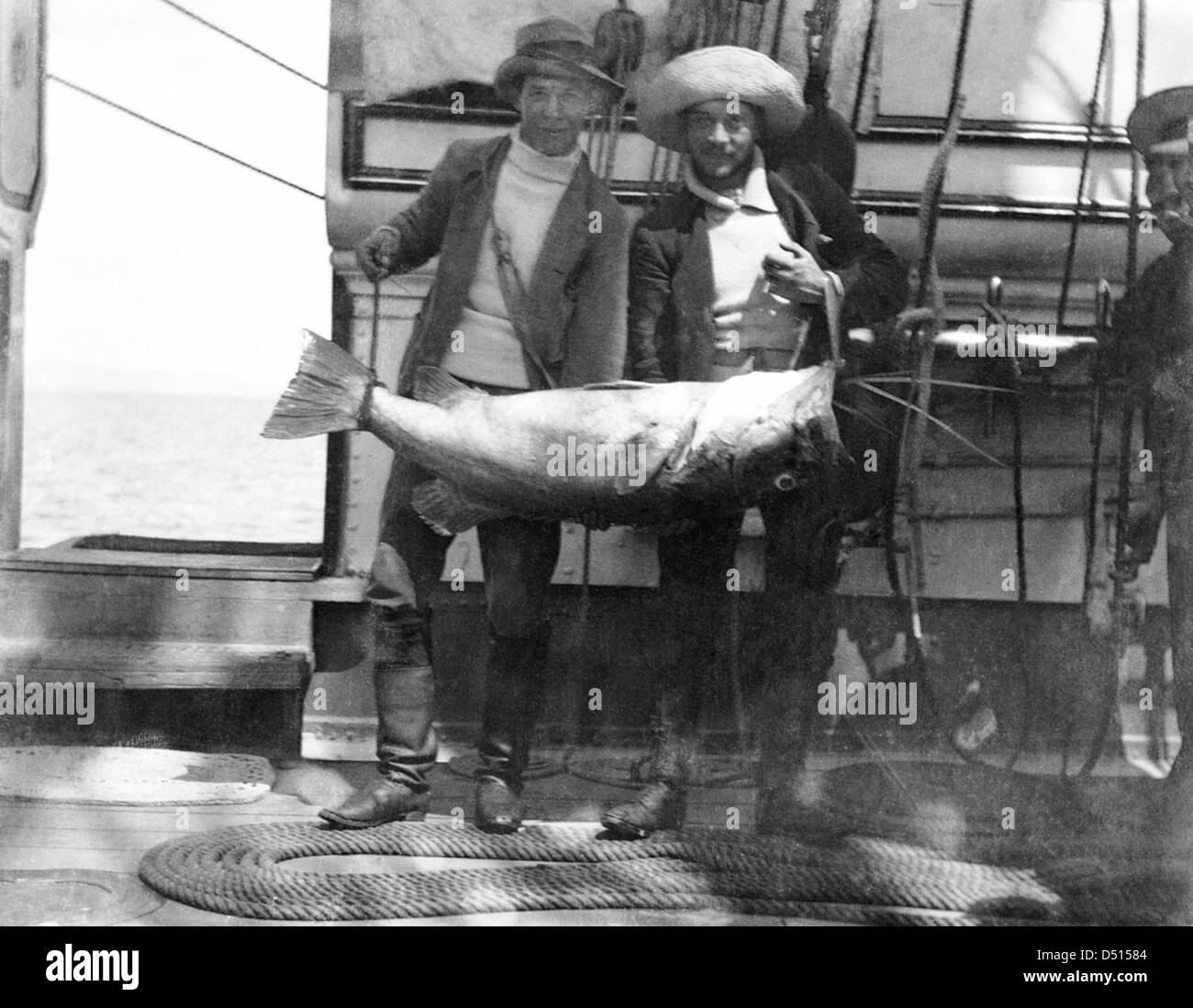 Cette photographie montre deux membres d'équipage à bord du HMS 'Penguin' avec un gros poisson qu'ils ont capturé. L'image, conservée par le Musée maritime national, illustre la vie en mer à l'époque de la voile. Banque D'Images