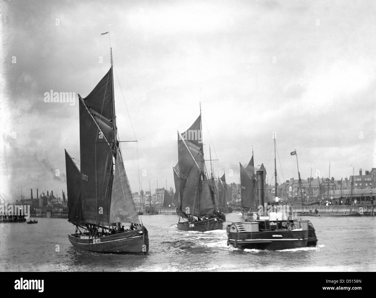 Cette photo montre le chalutier LT372 sous voile, remorqué par le remorqueur à aubes « Imperial » alors qu'il quitte le port. L'image capture un moment des opérations maritimes, mettant en évidence la coordination entre les navires à voile et les remorqueurs à vapeur. Banque D'Images