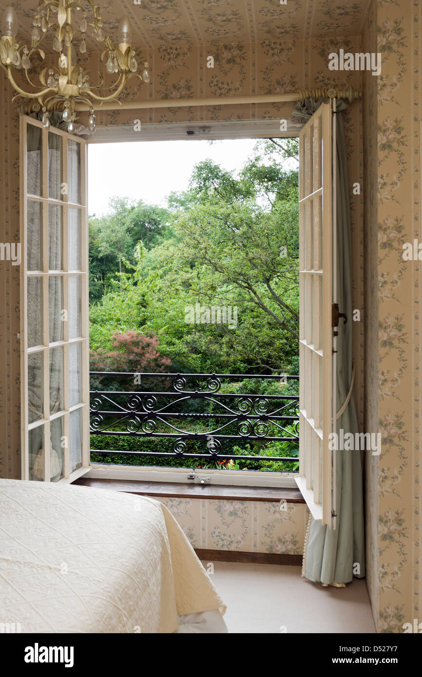 Vue d'une chambre à travers une grande fenêtre sur un jardin mature. Banque D'Images