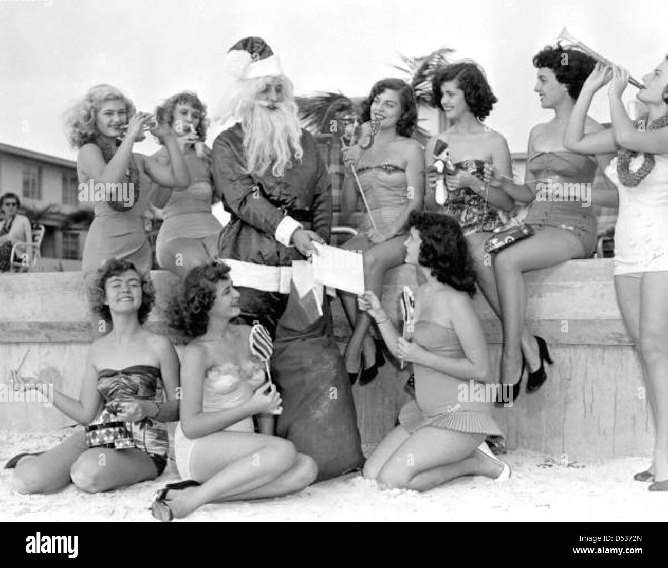 Le Père Noël distribue des friandises aux jeunes femmes sur la plage de Saint-Pétersbourg, en Floride, pendant la période des fêtes de Noël. La scène festive capture la joie et l'esprit de vacances des plages de Floride. Banque D'Images