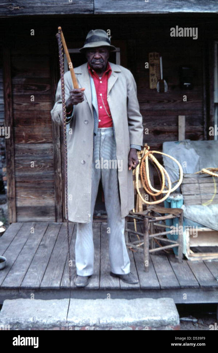Alvin Goodvine, un artisan de Lake City, en Floride, se tient debout sur son porche en tenant des fouets, mettant en valeur ses talents de maroquinerie. Cette image fait partie de la collection folk du comté de Columbia, mettant en valeur l'artisanat et les traditions locales. Banque D'Images