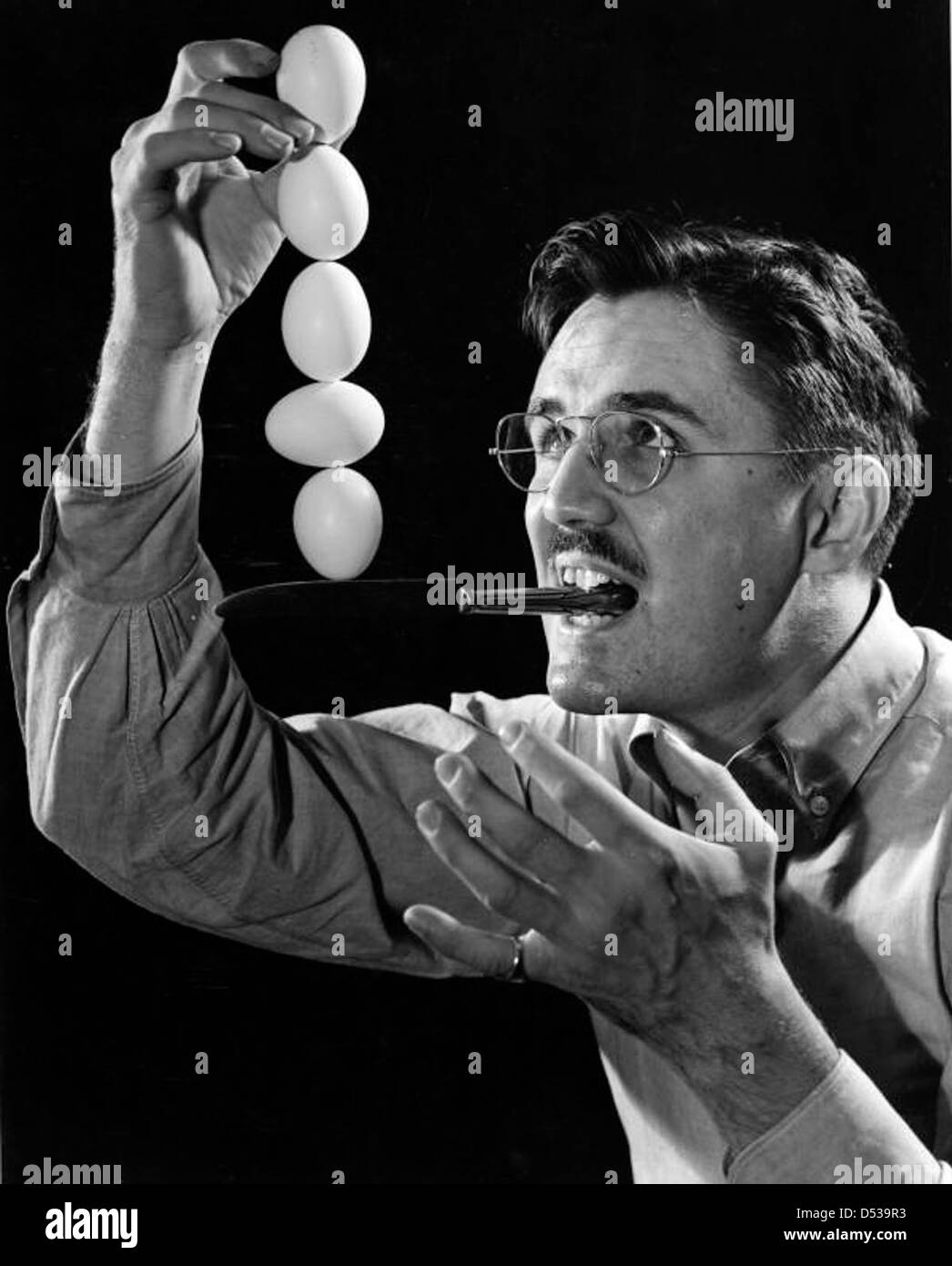 Joseph Steinmetz effectue un tour d'équilibrage des œufs dans les années 1930 Son acte, mettant en valeur son talent de magicien, est capturé avec une attention particulière aux détails, y compris sa moustache et ses lunettes distinctives. Banque D'Images