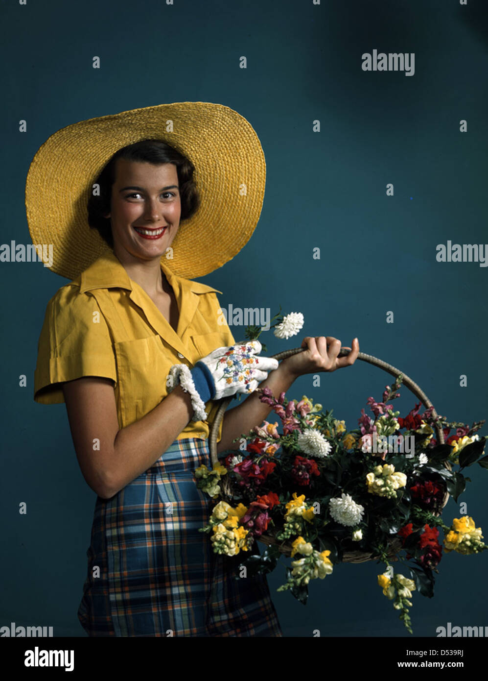 Un mannequin à Sarasota, en Floride, des années 1940, tenant un panier de fleurs, mettant en valeur la mode et la culture du jardinage à l'époque. Banque D'Images